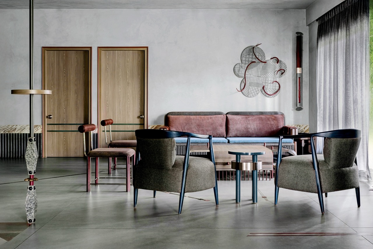 The living room of architect Smita Thomas’s grey-dominated duplex is large, spacious, and a microcosm of the materiality that is seen through the house. A four-seater custommade couch has stainless steel inlays, while the back wall has a flowerinspired metallic artwork with twisted attachments.. The light fixture next to it is made of stained wood and concrete, with its front and side buckled in leather belts. Large lounge chairs in blue and grey, and two compact chairs with cylindrical back supports and stainless steel legs, round out the seating arrangement