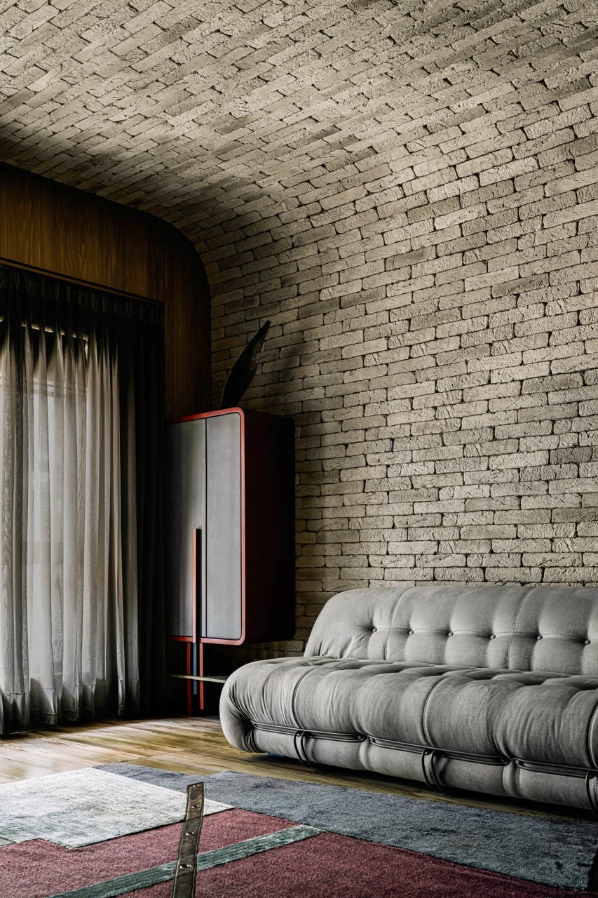 The TV and library room is a cocoon of comfort with a vaulted ceiling in weathered grey brick. Next to the couch is a customdesigned storage cabinet in deep burgundy with concretefinished shutters and a quirky slanting ear curving out from the top