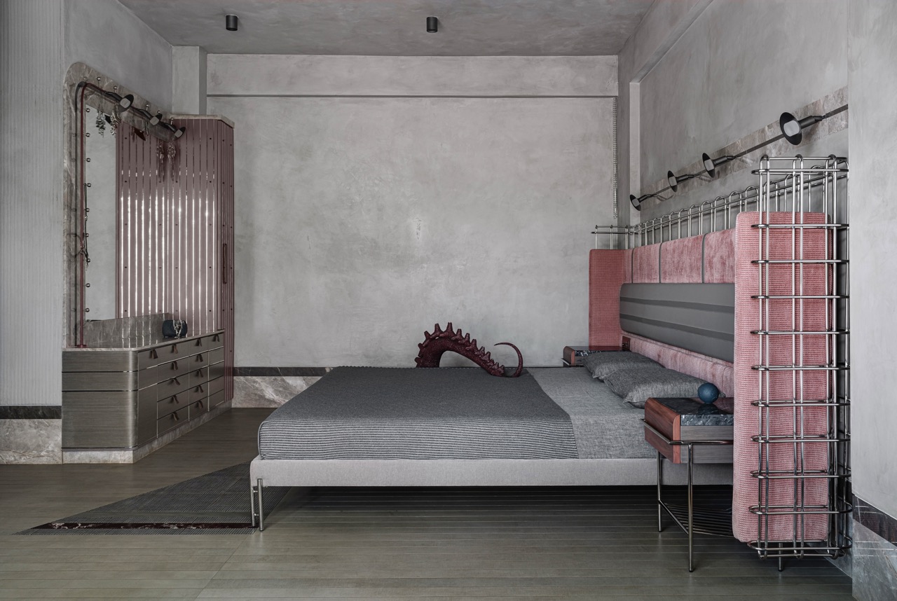 The headboard of this bed is almost like an installation of diverse materials. It features a lattice of stainless steel squares and a soft pink front with a horizontal strip of silver leather. The steel grid of the headboard stretches beyond the width of the bed to anchor the marble-topped nightstands