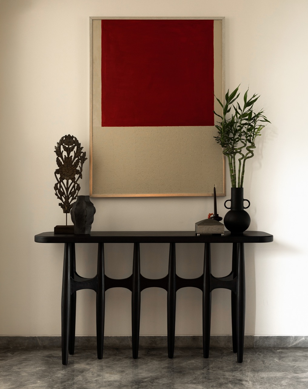 A vintage console paired with textured deep red artwork is layered with artefacts gathered over time in the foyer