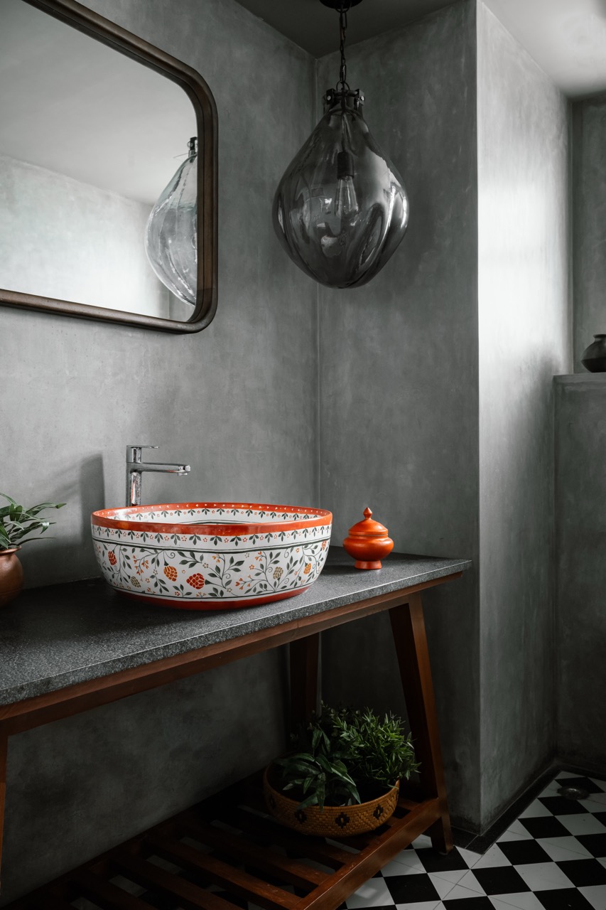 Grey IPS plaster walls meet a hand-painted ceramic basin by a ceramic artist Shibani, bringing a touch of Indian tradition to the powder room. A mirror by Ellementry, console table by ma+rs, and lighting by Orange Tree complete the look