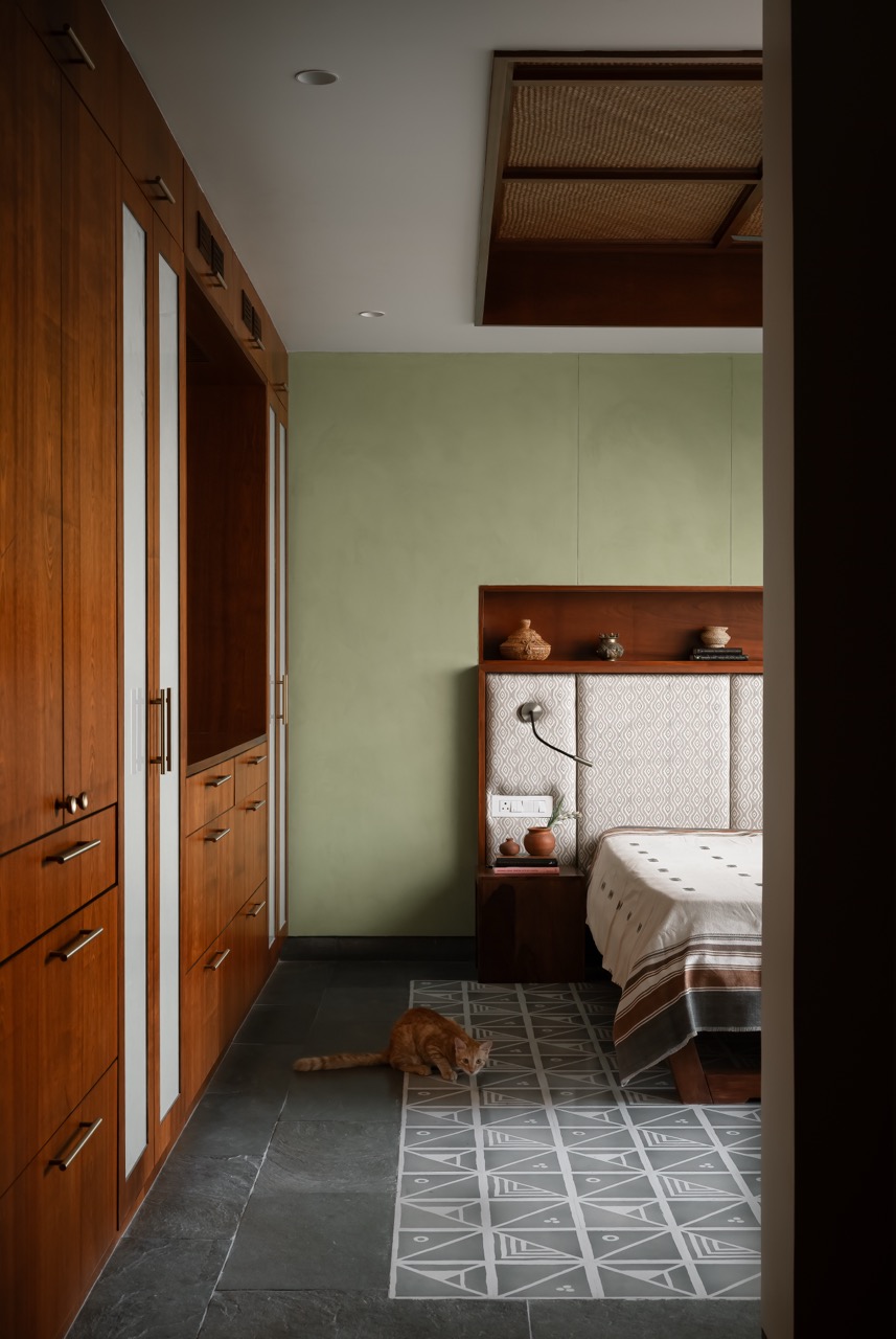 The primary bedroom has soft green lime-textured walls from Splash Textures and stone flooring with artisanal motif by Bharat Floorings & Tiles. The headboard fabric by Iqrup & Ritz adds a subtle touch