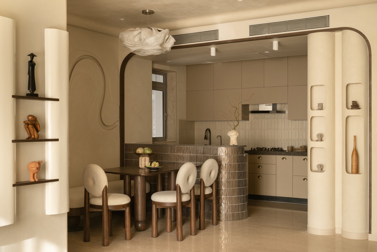 The open-plan layout furthers Rohini’s agenda for free-flowing spaces with the dining and kitchen areas separated by a curved kitchen island clad in metallic tiles. The wave motif makes a subtle appearance on the dining room wall. The table, chairs, and bench are by Anthem Home