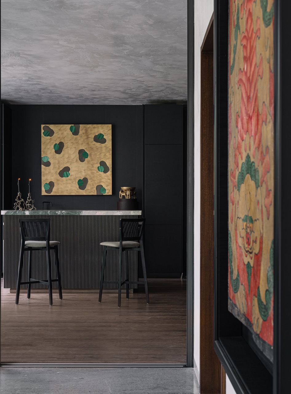In the entertainment room, dramatic black offsets the grey tones everywhere else. Decor elements feature a brass-inlay panel by Scarlet Splendour on the wall and an Elephant Dhoop table by Ashiesh Shah Atelier with candle stands by Viya Home placed on top. To the right is an antique Tibetan door with a silk border from antiques dealer Beg Borrow Steal