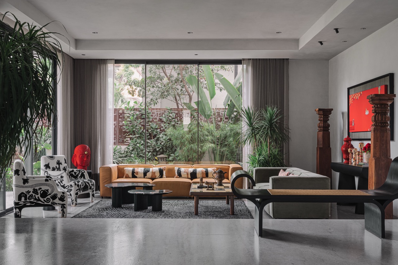 The formal living room looks out to the outdoors, which was landscaped by Pinewood Studio. The space is furnished with a tan-coloured sofa from BoConcept with armchairs and a black bench from Within Design