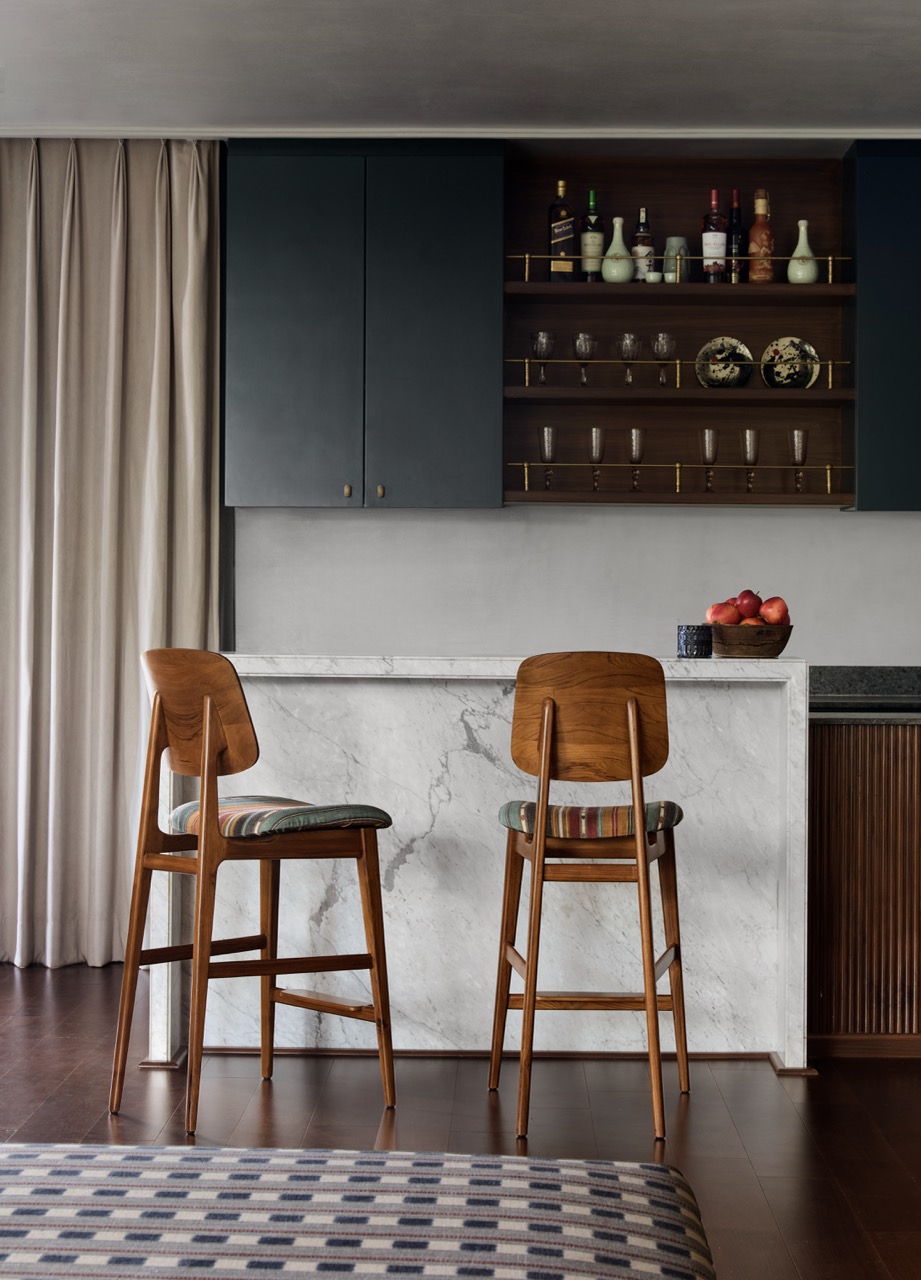 The bar showcases millwork, stone, and custom brass crafted by Niche Build Solutions, paired with Dastkari chairs upholstered in Studio Orion fabrics. Curtains by Drapes N’ More softly frame the space
