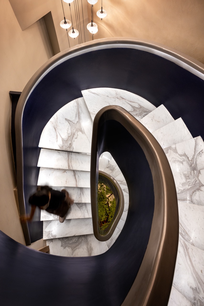 A spiral staircase marks the threshold, stitching together the stilt, basement, and upper ground floor through a single curved gesture