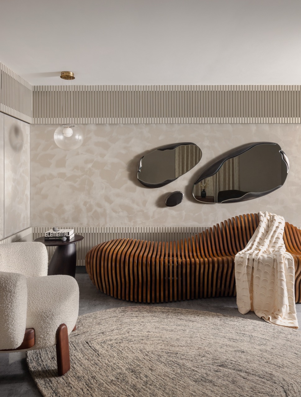 A calm seating nook pairs Sirca wall finishes with a fluid mirror by White Domus, grounded by a rug from Jaipur Rugs
