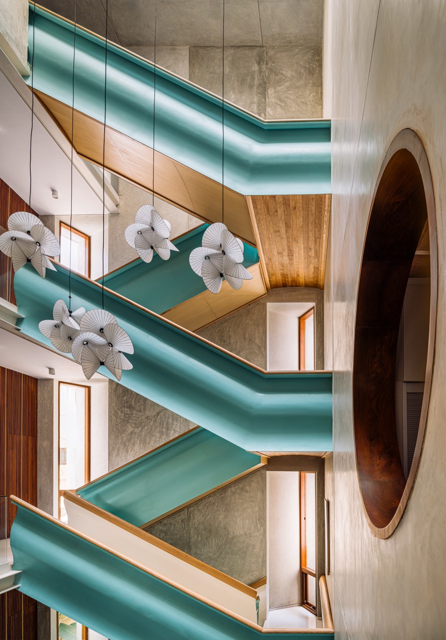 The atrium looks onto a metal staircase with marble treads and risers, set against white and grey oxide walls. A hanging light by Moooi anchors the vertical space
