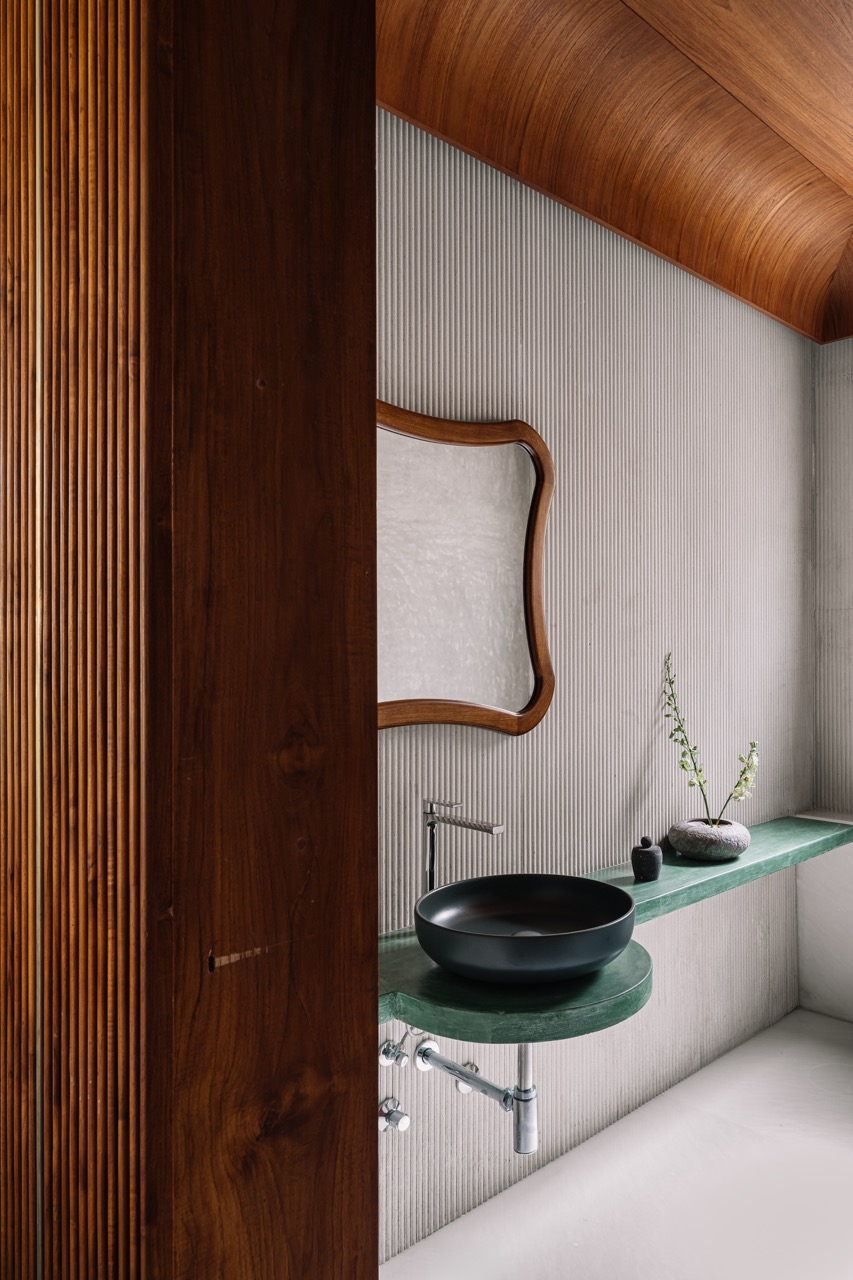 The powder room pairs fluted white marble with oxide-finished walls and a wooden ceiling. A green oxide counter and basin from Style Box add contrast