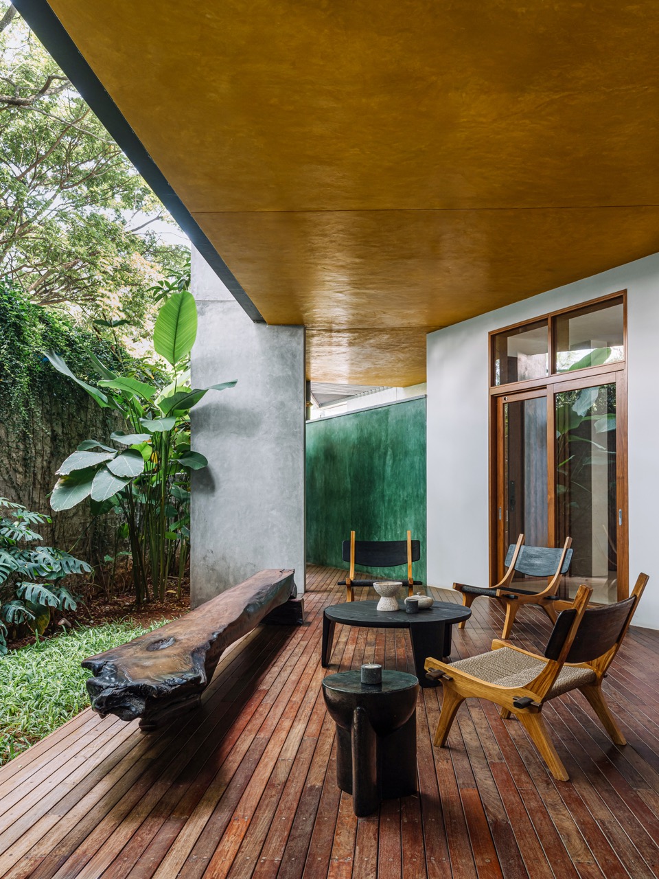 The deck opens to a green patch, with furniture by Kayu and wood flooring that blends into the landscape. The ochre ceiling and green corrugated wall at the far end complements the earthy nature of the space