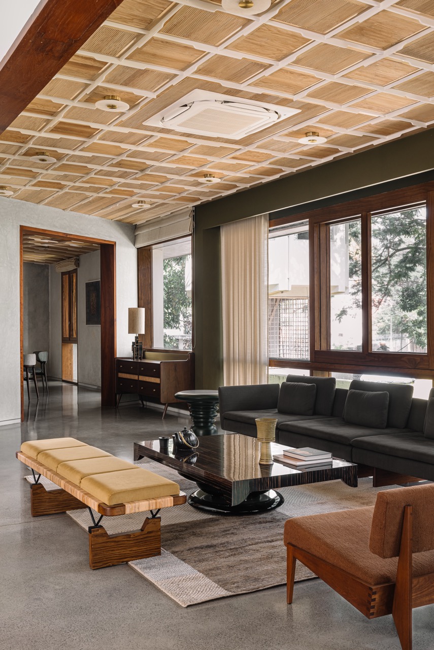 The living room opens toward the dining area, with furniture by AAD (Amaresh Anand Designs) in collaboration with Magari, Phantom Hands, and Timberworks India by Virasp Bativala, set against concrete flooring by AAD and Living Elements