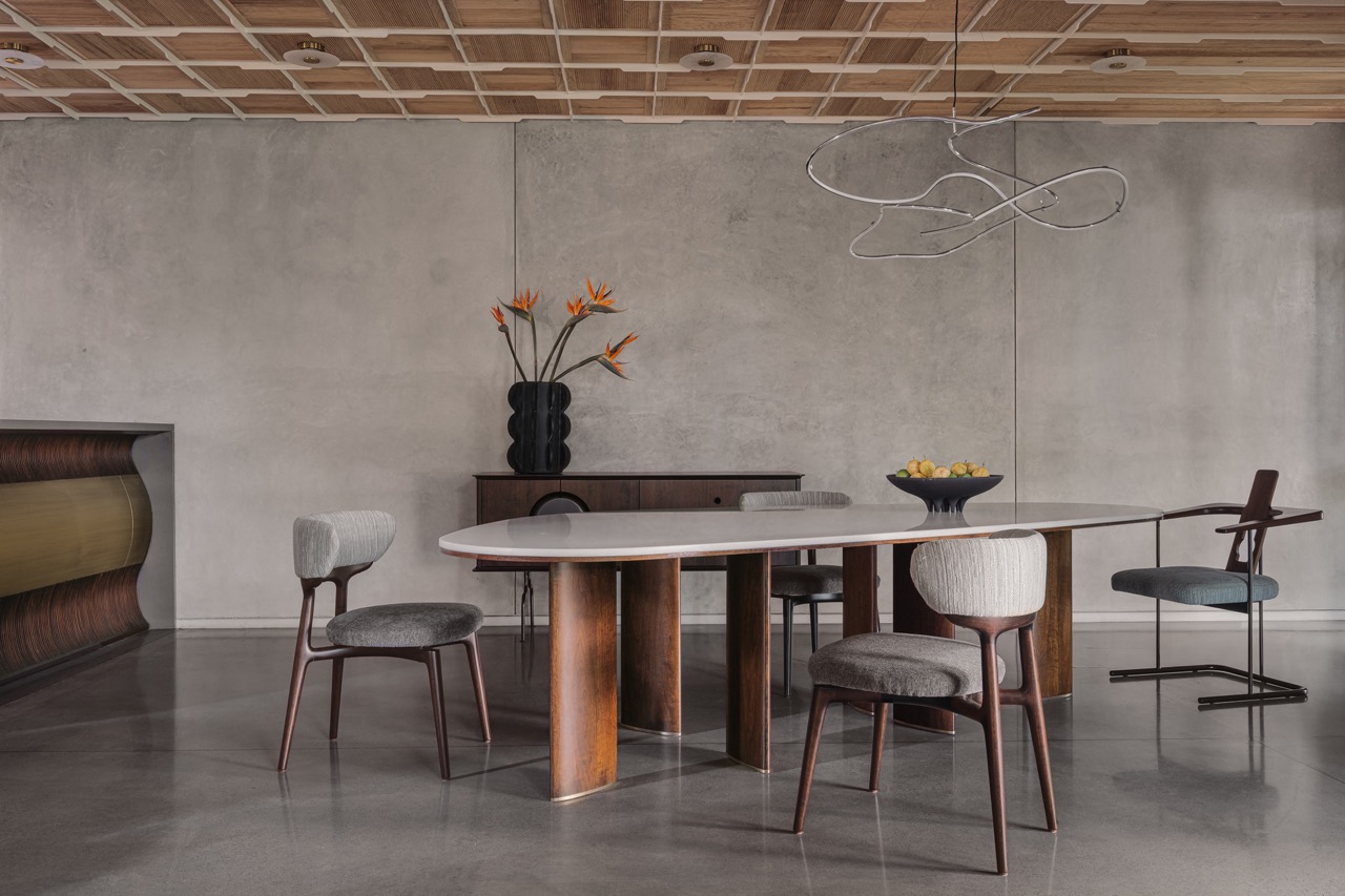The dining area extends into the open kitchen, where grey oxide walls and concrete flooring by AAD and Living Elements continue the material palette. Furniture by Timberworks India by Virasp Bativala and a light by 101 Copenhagen complete the space